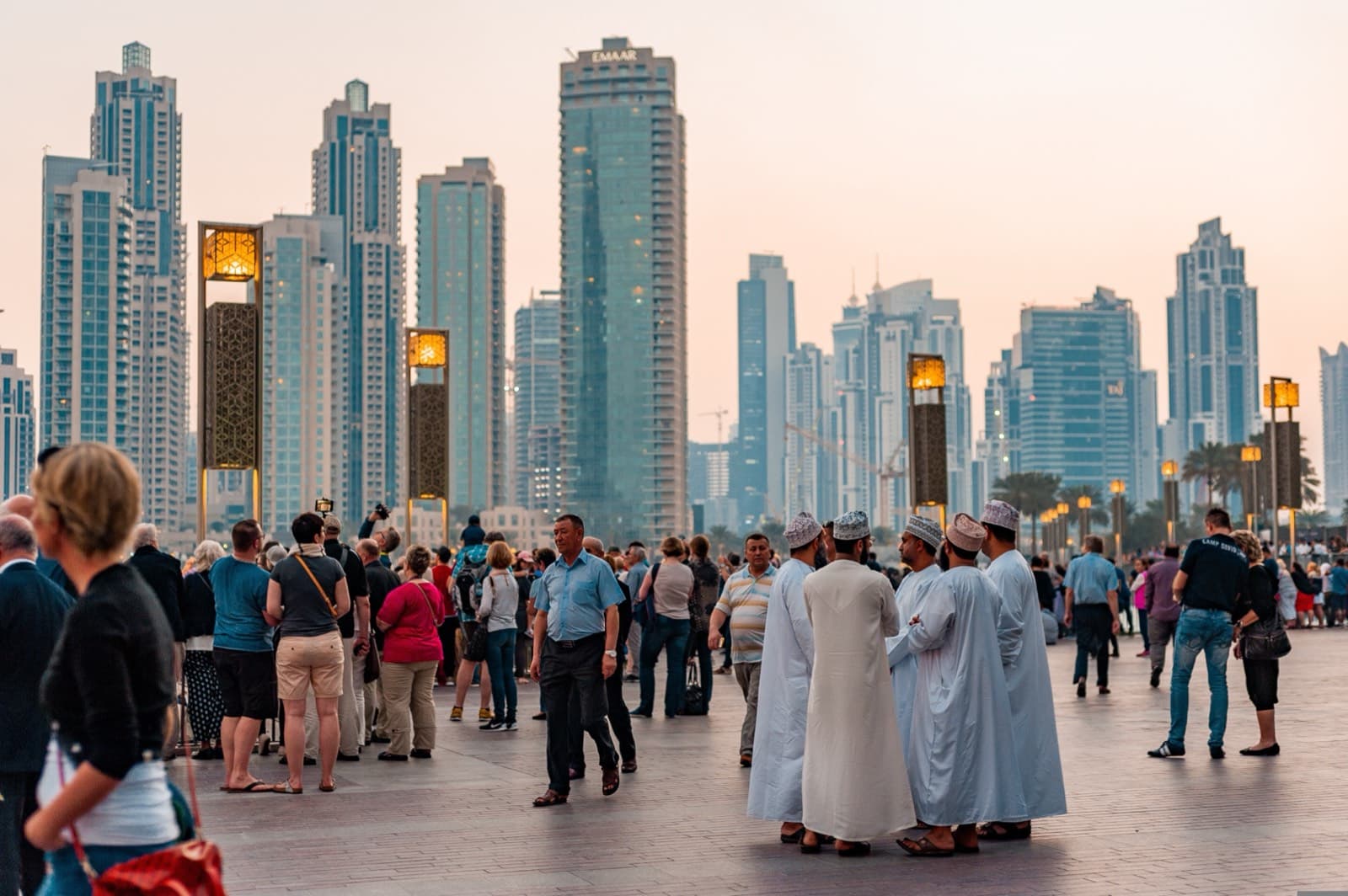 Promenáda v Downtown Dubai s místními muži v tradičních kandurách a panoramatem mrakodrapů