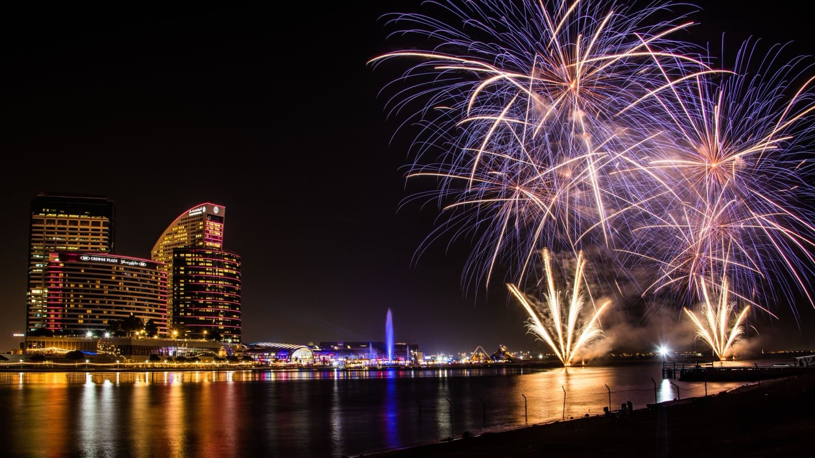 Ohňostroje nad nábřežím Dubai Festival City s osvětlenými hotely odrážejícími se ve vodě