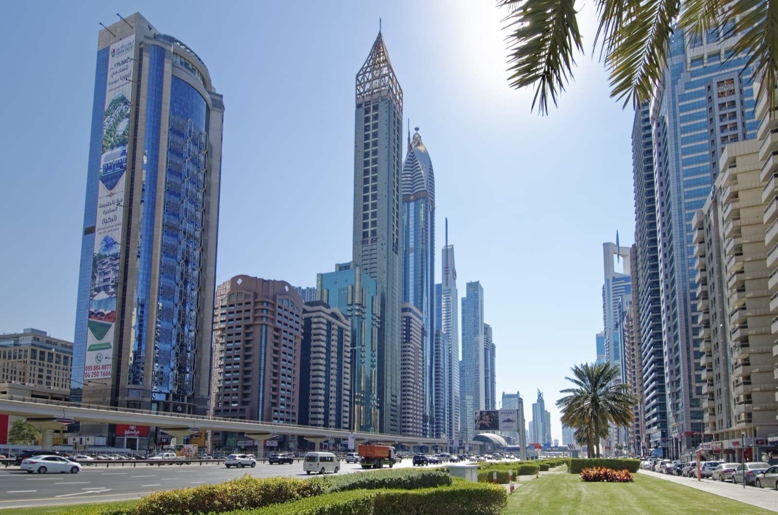 Slunečný den na Sheikh Zayed Road v Dubaji s mrakodrapy a palmami